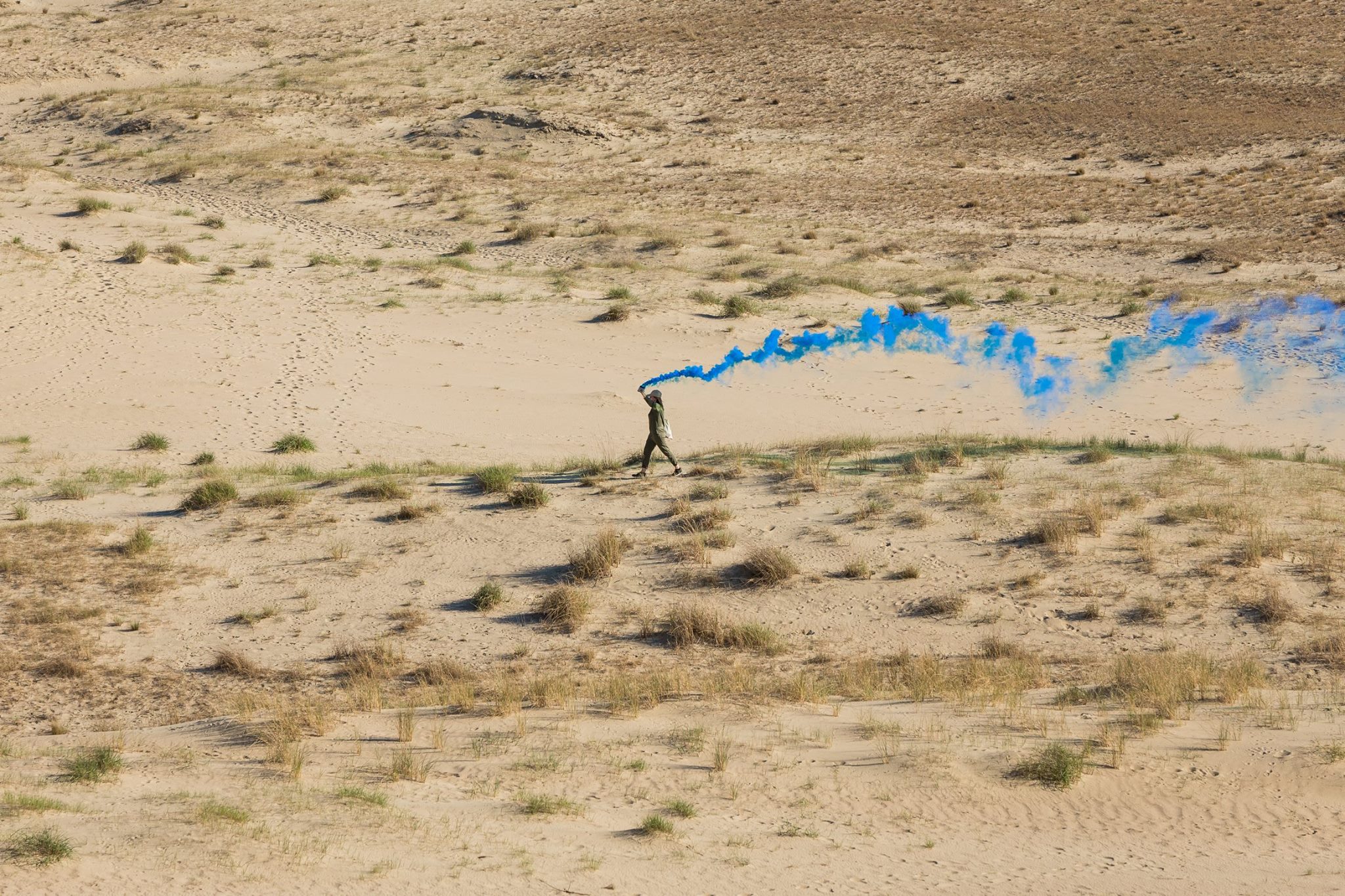 Still from performance of smoke walk, Nida, Lithuania. The artist walks across a sand dune landscape with a blue smoke fare describing the path already walked